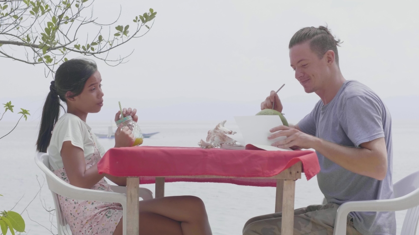 Inlove couple smiling and reading story in book while drinking fresh juice.
