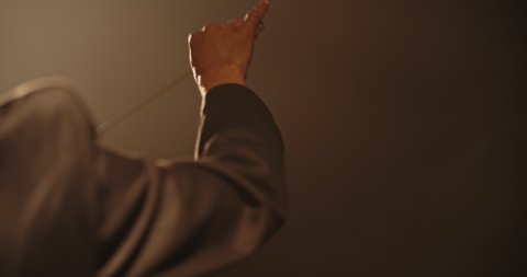Close up shot of hand of unrecognizable orchesra conductor waving his stick and directing musicians during a rehearsal. Studio shot on black background 4k footage