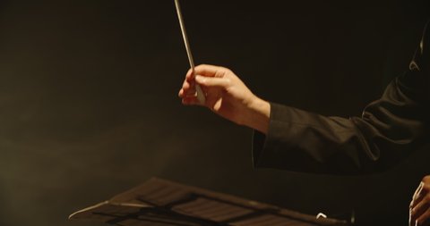 Close up shot of hands of symphony orchesra conductor directing music by waving his baton. Studio shot on black background 4k footage
