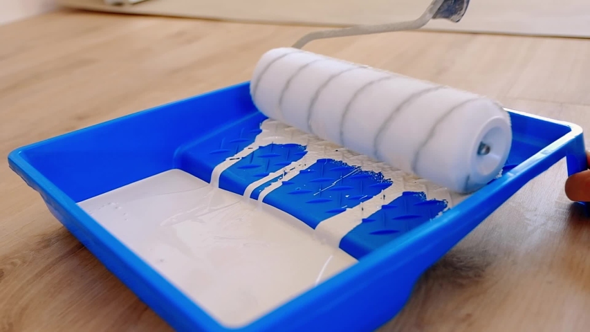 The builder dips the roller in the paint and rolls it along the wall of the tray