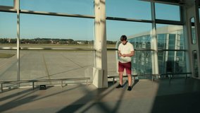 man with beard, stands at airport by window, holding passport, waiting for plane
