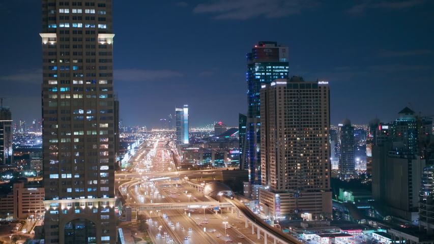 Skyline internet city with crossing Sheikh Zayed Road aerial night view. Illuminated skyscrapers with traffic on a highway and metro line in Dubai
