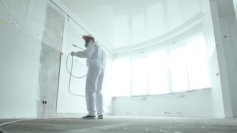 Painter works with airless spray gun when painting ceiling