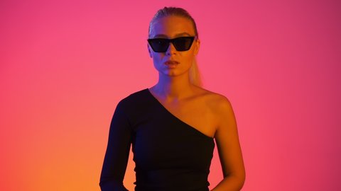 Attractive caucasian blonde young girl doing hush shh! sign with finger on lips, looking seriously to camera. Gesture of silence in vivid neon light with red and blue colors at gradient background