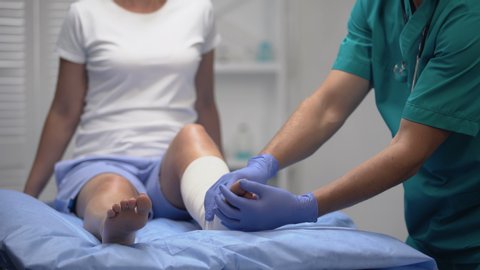 Orthopedist fixing elastic warp on patients leg after sport trauma, healthcare