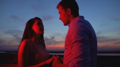 Young couple holding hands on terrace at night breaking up, misunderstanding