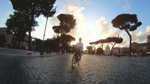 Young woman riding a bike in Rome at sunset. Beautiful elegant white dress and skirt. Camera dolly shot. Olga_Colosseo_