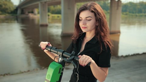 beautiful young girl stands with electric scooter by river and bridge