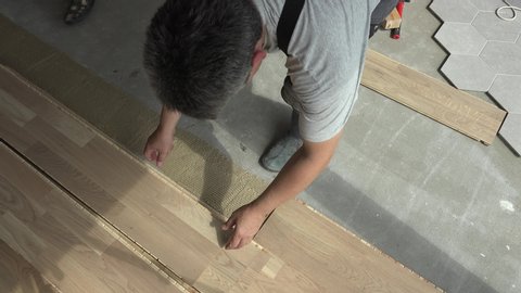 Professional workers lay oak floor boards. New apartment finishing works. Static closeup shot.