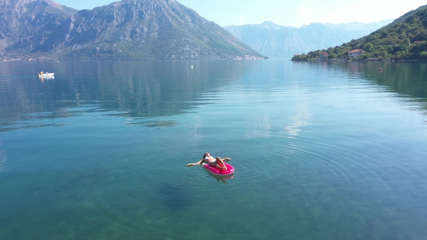 AERIAL. Young women enjoy floating on a mattress at the sea. Mountains on background.