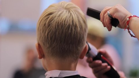 Hairdresser cuts hairs with clipper on boy's head.