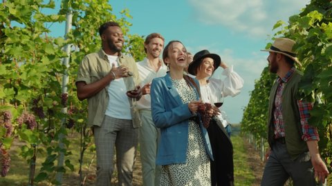 Fun young farmer guiding exciting wine tour for wealthy people. Happy mixed race friends laughing of joke reveling in holiday vacation to vineyard.