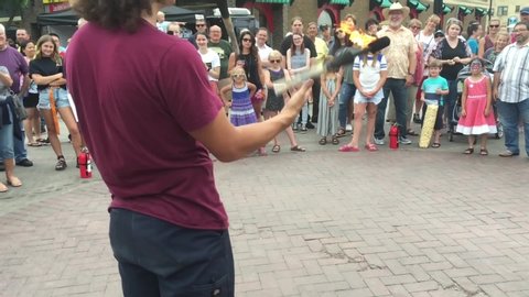 August, 2019 - Fargo, ND:  Street performer juggles fire in slow motion with fair patrons happily looking on to his talents. 