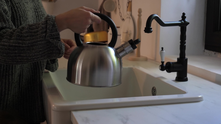 woman fill in water from a faucet to a kettle