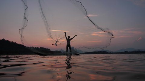 Slow Motion Silhouette of fishermen throwing fishing net during sunset with boats at the lake. Concept Fisherman's life style. Lopburi,  Asia, Thailand. 