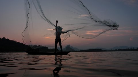 Slow Motion Silhouette of fishermen throwing fishing net during sunset with boats at the lake. Concept Fisherman's life style. Lopburi,  Asia, Thailand. 