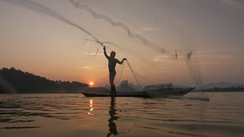 Silhouette of fishermen throwing fishing net during sunset on boat at the lake. Concept Fisherman's Lifestyle in countryside. Lopburi, Thailand, Asia.