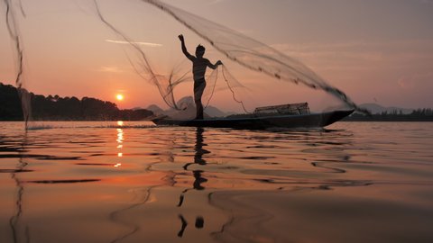 Slow Motion Silhouette of fishermen throwing fishing net during sunset on boat at the lake. Concept Fisherman's life style. Lopburi,  Asia, Thailand. Slow Motion