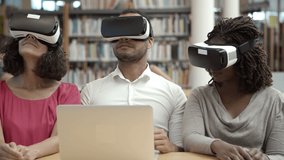 Slow motion of three testers with VR headsets. Concentrated people sitting at library with modern devices. Technology concept