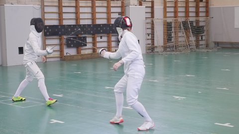 Two young women having an active fencing training in the school gym