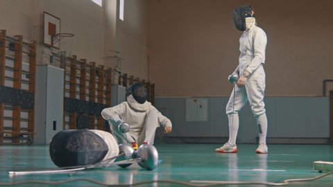 Two young women fencers having a training in the gym - giving a hand to help to stand up
