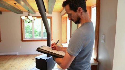 Indoor damp & air quality (IAQ) testing. A closeup view of a caucasian building inspector at work, using a pen and notepad to carry out an assessment inside the family room of a residential home.