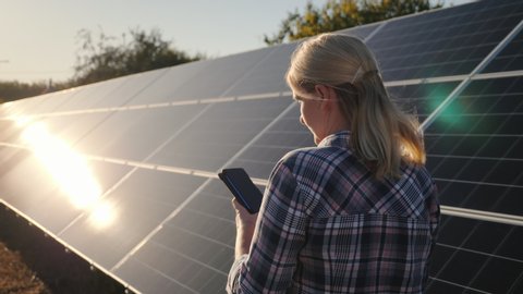 Bakc view of Woman with smartphone goes aquarius solar panels at home solar power plant