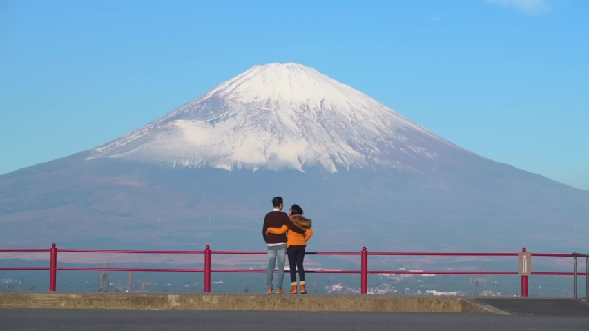 Two Asian adutls hug each other looking at Mt. Fuji in Japan. Concept of couple lovers travel to Japan for honeymoon. 