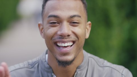 Handsome black male reacts and laughs at something as he looks to camera, in slow motion
