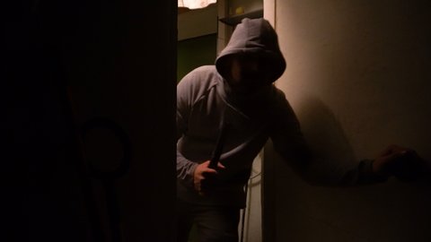 A man in a sweatshirt holds an ax in his hand. Evil look. Bad intentions. Enters the door. The interior of the garage. Close-up.
