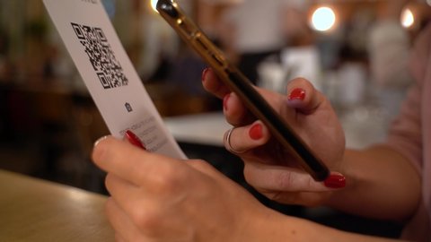 Scanning QR code with smart phone. The woman reads the bar code using the application on the smartphone in cafe