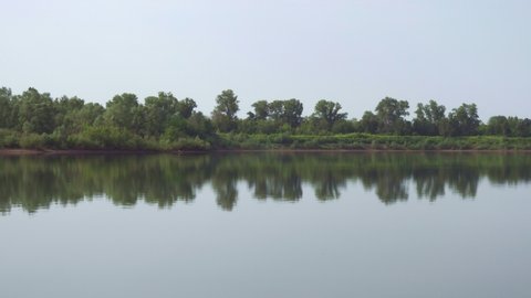 Shooting from a tripod on the shore of a pond. A view of the calm expanse of water and the opposite shore with dense vegetation. Trees and sky are reflected in the water.
