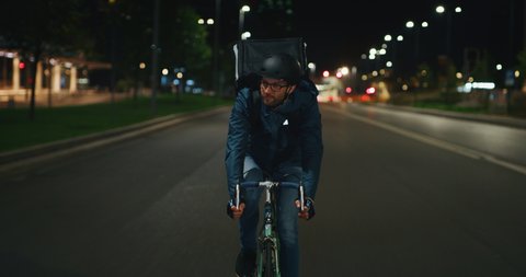 Slow motion of an young courier wearing a security helmet is making a delivery of the order to the customers by bicycle in the evening in a city center.