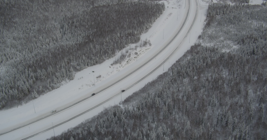 Aerial helicopter shot, above snowy Alaskan highway, trucks, cars drive past, tilt up to see suburban area, houses, drone footage