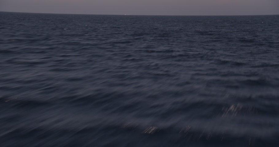 Helicopter aerial shot tracking quickly over dark blue ocean, evening
