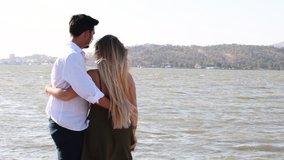 Happy couple looking into the ocean. Caucasian blonde woman and Turkish (Middle Eastern) man in love at the waterfront in Izmir in Turkey. Wife and husband enjoying the view of the ocean. 4K video.