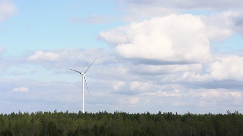 Wind farm, single wind turbine, standing tall over pine forest in Finland, on a beautiful day with a white clouds filled sky.