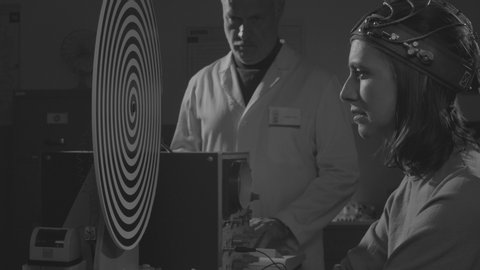 Vintage style scientist hypnotizing a woman in the lab, she is wearing a helmet and staring at the spinning spiral