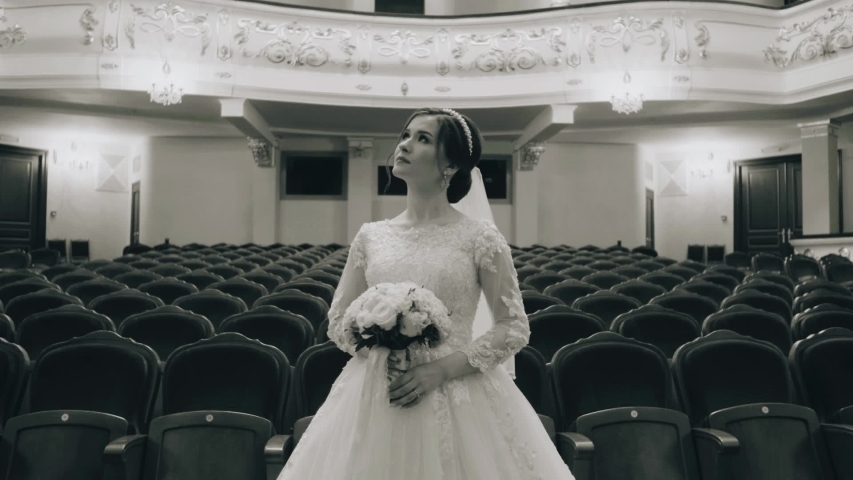 A girl in a snow-white dress stands in the middle of the auditorium at the Opera. The camera is in motion. It
