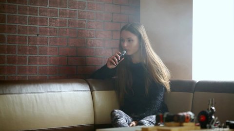 Vape teenager. Young pretty white caucasian girl with long hair smoking an electronic cigarette in vape bar. Bad habit that is harmful to health. Vaping activity.