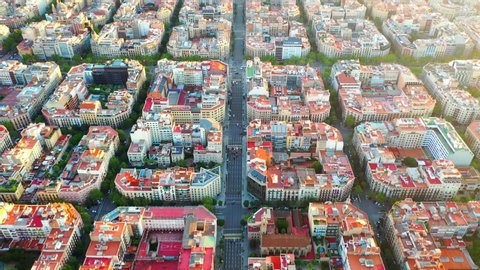 Aerial, tilt up, drone shot, over streets and blocks, full of buildings, revealing the sunset, over the cityscape of Barcelona city, on a sunny, summer evening, in Catalonia, Spain