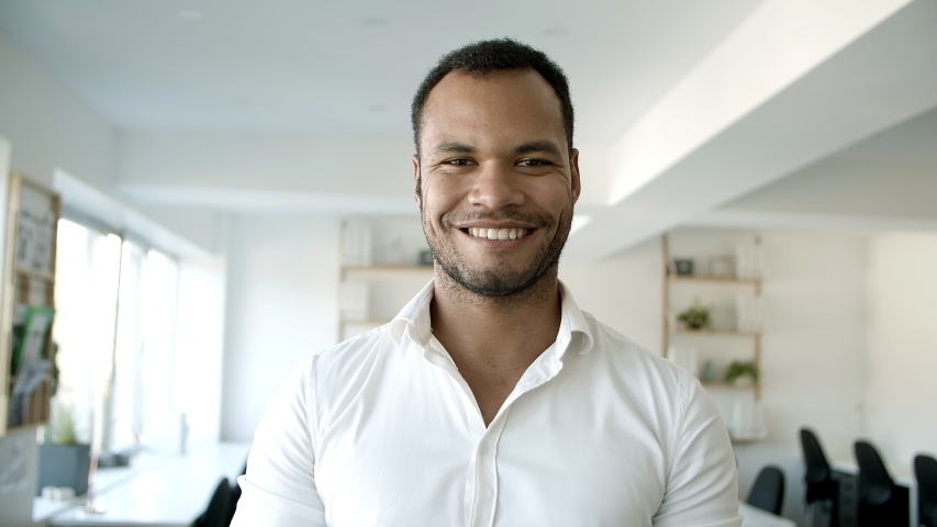 Young bearded guy standing with crossed arms at office. Front view of confident African American man looking at camera. Concept of confidence