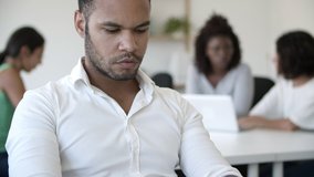 Concentrated African American employee typing on laptop. Front view of focused young man working with modern device. Technology concept