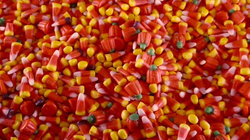 A hand is seen grabbing into a large pile of Halloween candy corn and pumpkins.