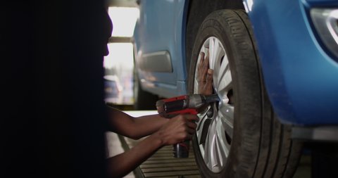 4K Beautiful African American mechanic replacing a car tire in garage workshop. Slow motion.