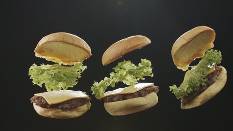 Ready burgers fly up on a black background. Slow motion video
