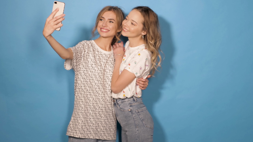 Two beautiful smiling girls.Women in summer hipster clothes taking selfie self portrait photos on smartphone. Models making funny faces and having fun in studio.They show tongue and make duck face