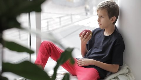 boy eats a red Apple sitting on the windowsill in the room