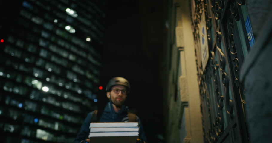 Slow motion of an young pizza courier is delivering an order to and a customer is using a smartphone for mobile pay in the evening in a city center. Royalty-Free Stock Footage #1038586655