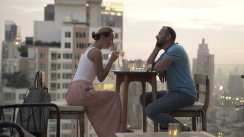 Young couple relaxing, talking and drinking cocktails in bar on terrace